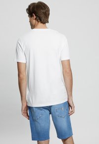 Witte katoenen T-shirt met korte mouwen, rechte snit, gecombineerd met blauwe denim shorts met voorkezen en een rafelrand.