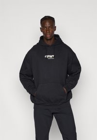 Sudadera negra con capucha y bolsillo tipo canguro, con un logo blanco en el frente y en el centro, hecha de un material suave y con un corte relajado.