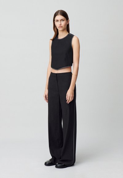 Top de tanque negro recortado con dobladillo en punta, combinado con pantalones negros de pierna ancha de tiro alto que presentan piping lateral y acentos de hardware mínimos.