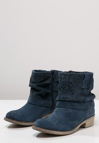 Ciemnoniebieskie zamszowe botki za kostkę z teksturowanym designem, z wycinanymi detalami i beżowym, grubym, niskim obcasem.