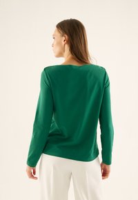 Lange mouwen groene top van zachte stof, met een vierkante halslijn en een relaxte pasvorm, met een gladde textuur en minimalistisch ontwerp.
