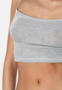 Hõbedane lühike tank top õhukeste rihmadega, valmistatud tekstureeritud, metallik kudumkangast. Sile viimistlus ja keha lähedane disain.