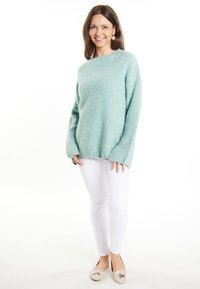Helles blaues, gestricktes Sweatshirt mit lässiger Passform, langen Ärmeln und strukturiertem Rippenmuster, kombiniert mit weißen engen Hosen und hellen Flats.