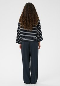 Marineblå langærmet top med striber og vide ærmer, kombineret med løstsiddende mørke bukser. Begge beklædningsgenstande har en afslappet silhuet.