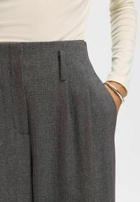 Pelēkas piegrieztas bikses ar teksturētu audumu, priekšpusē ar krokām un sānu kabatām. Kombinētas ar pieguļošu krēmkrāsas garumu piedurkņu topu.