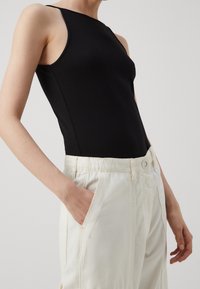 Czarny bezrękawnik wykonany z gładkiego materiału, w połączeniu z luźnymi off-white spodniami z bocznymi kieszeniami i prostym wzorem pasa.
