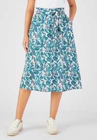 Jupe midi imprimée florale en teal et blanc, avec une taille élastique et une ceinture nouée. Le tissu est léger et fluide. Associée à des baskets blanches.