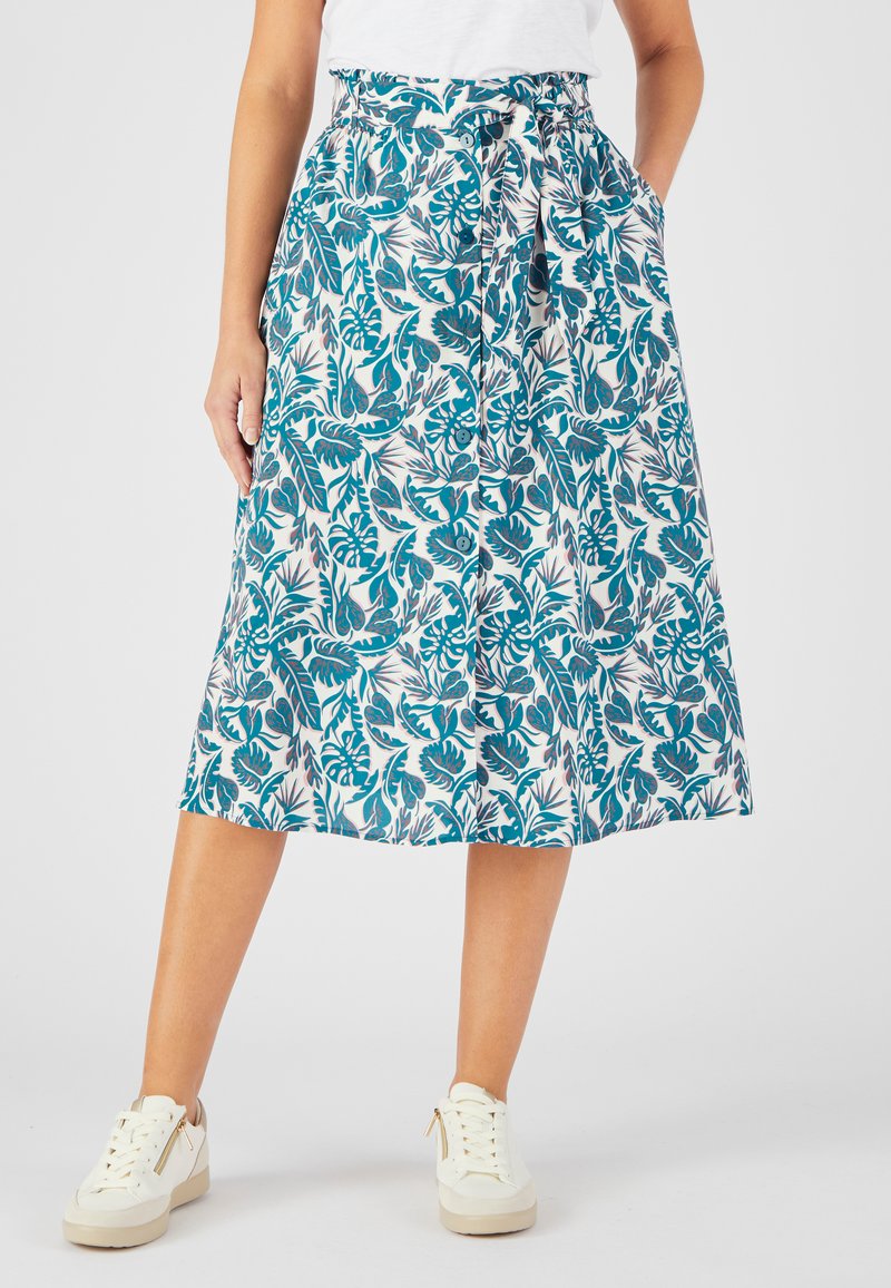 Jupe midi imprimée florale en teal et blanc, avec une taille élastique et une ceinture nouée. Le tissu est léger et fluide. Associée à des baskets blanches.