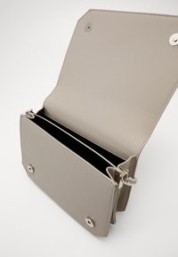 Lysegrå skuldertaske i syntetisk læder med klaplukning. Har sølvfarvede metaldele, to indvendige rum og en tekstureret yderside.