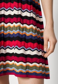 Vestido de punto con vibrantes rayas en zigzag en rojo, negro, blanco, verde, azul y naranja. Tejido ligero con una textura suave.