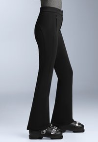 Fekete harangszárú nadrág rugalmas anyagból, két oldalsó zsebbel, kiemelkedő varrásokkal, fekete sícipővel, ezüst bucklékkal viselve.