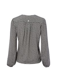 Achteraanzicht van een blouse met lange mouwen in een zwart-wit stippenpatroon, voorzien van een ronde halslijn en subtiele plooien aan de achterkant.