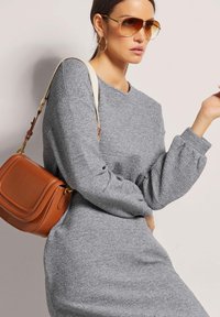 Graues Strickkleid mit voluminösen langen Ärmeln, einem runden Ausschnitt und einer figurnahen Silhouette. Braune Leder-Crossbody-Tasche mit goldenen Beschlägen.
