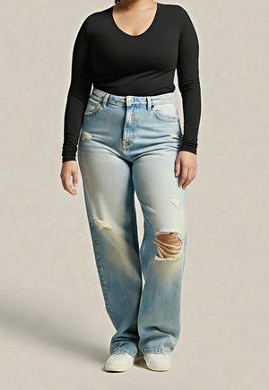 Person wearing light blue ripped jeans and a black long-sleeve top, standing with hands relaxed by sides against a neutral background.