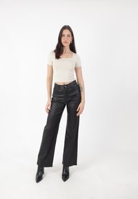 Zwarte nepleren broek met wijde pijpen en hoge taille, gecombineerd met een fitted crèmekleurig top met korte mouwen. Model draagt puntige zwarte enkellaarsjes.