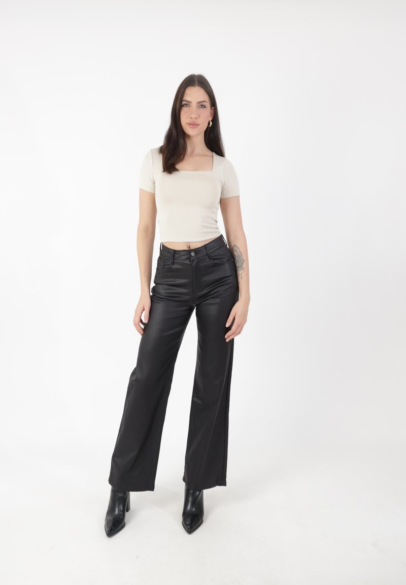 Pantalones de cuero sintético negros de pierna ancha con cintura alta, combinados con una blusa ajustada de manga corta en color crema. El modelo lleva botines negros de tacón puntiagudo.