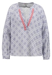 Långärmad vit blus med blå geometriska mönster och en röd mönstrad V-ringning.