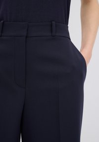 Marinblå byxor med en slät textur, som har en skräddarsydd passform, sidfickor och en platt midja för en strukturerad look.