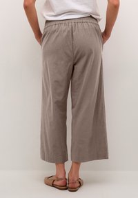 Pantalons large couleur marron clair avec une taille élastique et un tissu texturé. L'ourlet est droit, et ils descendent jusqu'au mollet.