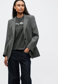Gray pinstriped blazer with notched lapels over a dark gray t-shirt featuring white text. Worn with dark denim pants. Smooth texture.