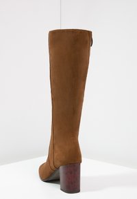 Botte hauteur genou en daim marron avec un bout arrondi et un talon bloc épais au motif écaille. Texture lisse, design élégant, sans éléments métalliques visibles.