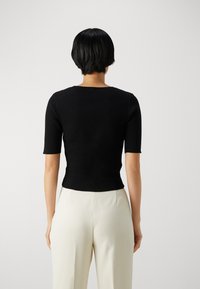 Top negro de manga corta con canalé, escote redondo, diseño ajustado y tejido texturizado, combinado con pantalones color crema.