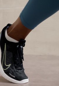 Fekete sportcipő csíkozott mintával, fehér részletekkel és fekete fűzővel. A cipő rugalmas talppal rendelkezik, és szoros illeszkedést biztosít a bokán.