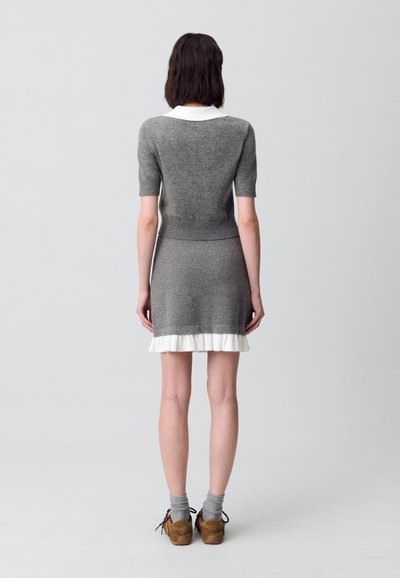 Vestido de punto gris con mangas cortas, un cuello blanco y un dobladillo con volantes. Textura suave y silueta ajustada, combinado con zapatos de plataforma marrones.