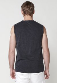 T-shirt sans manches gris foncé avec col rond, fabriqué à partir d'un tissu doux. Présente un ourlet droit et des coutures visibles le long de l'encolure.