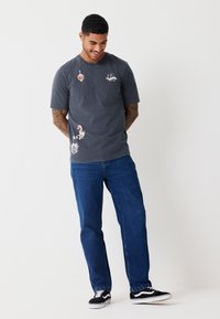 Gray cotton t-shirt with round neckline, featuring colorful graphic prints. Paired with blue straight-leg jeans and black sneakers.