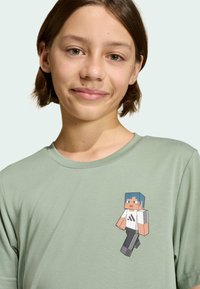 Svetlozelené bavlnené tričko s potlačou postavy z Minecraftu, ktorá má modré vlasy, oblečenú bielu košeľu s čiernymi prúžkami a šedé nohavice.