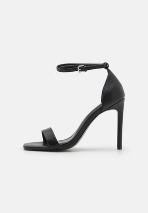 Čierne sandále na vysokom opätku s elegantným dizajnom, obsahujúce popruh okolo členka, otvorenú špičku a hladký kožený povrch.