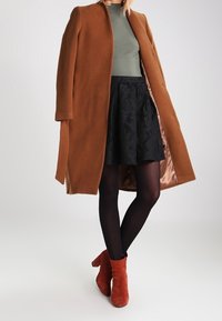 Brown wool coat, green top, black skirt, black tights, and red ankle boots. Coat has a streamlined design with buttons and satin lining.
