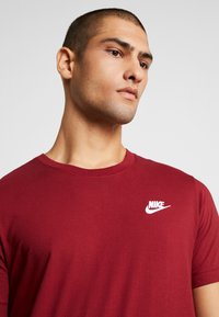 Bordo tričko s krátkymi rukávmi a okrúhlym výstrihom z bavlny, s bielym logom Nike na ľavej strane hrudníka. Hladká textúra.