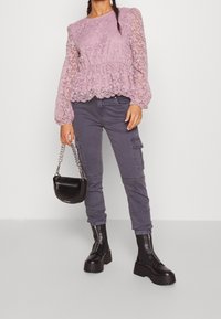 Top peplum in pizzo viola chiaro con maniche lunghe, abbinato a pantaloni cargo grigi e stivali platform neri chunky. Include una piccola borsa nera.