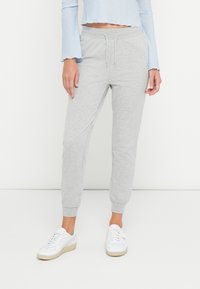 Lichtgrijze sweatpants met een tailleband met trekkoord, elastische boorden en zijzakken. Gecombineerd met witte sneakers voor een casual look.