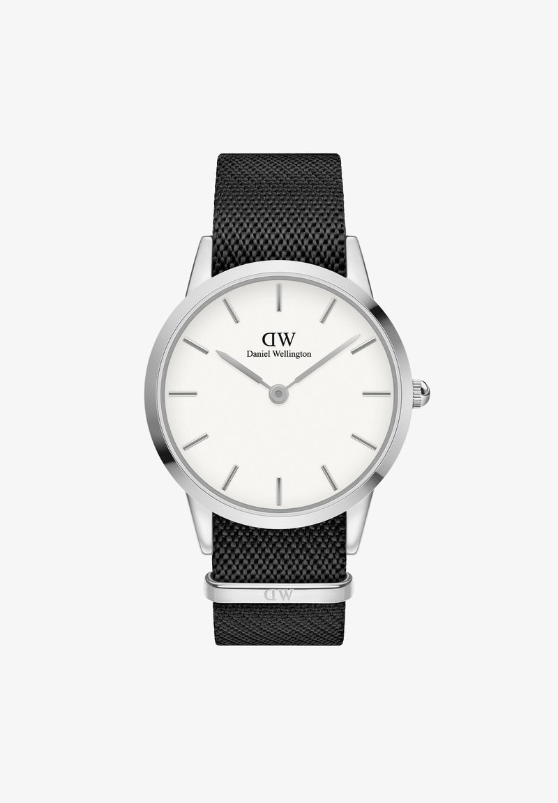 Hõbedane roostevabast terasest kell valge põhimõttega näo, musta võrgutööriistaga, ja minimalistikud tunni markerid. Näol ja rihmal on logo.