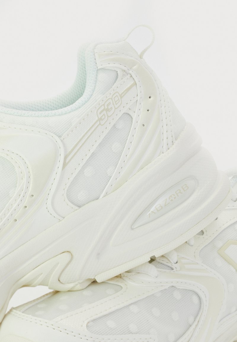 White sneakers with a textured mesh upper, dotted pattern, and reinforced rubber sole. Features include a padded collar and "ABZORB" branding.