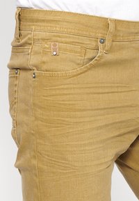 Rumene jeans iz bombažnega mešanega materiala ožjega kroja, z teksturirano površino, sprednjimi žepi in oznako blagovne znamke na pasu.