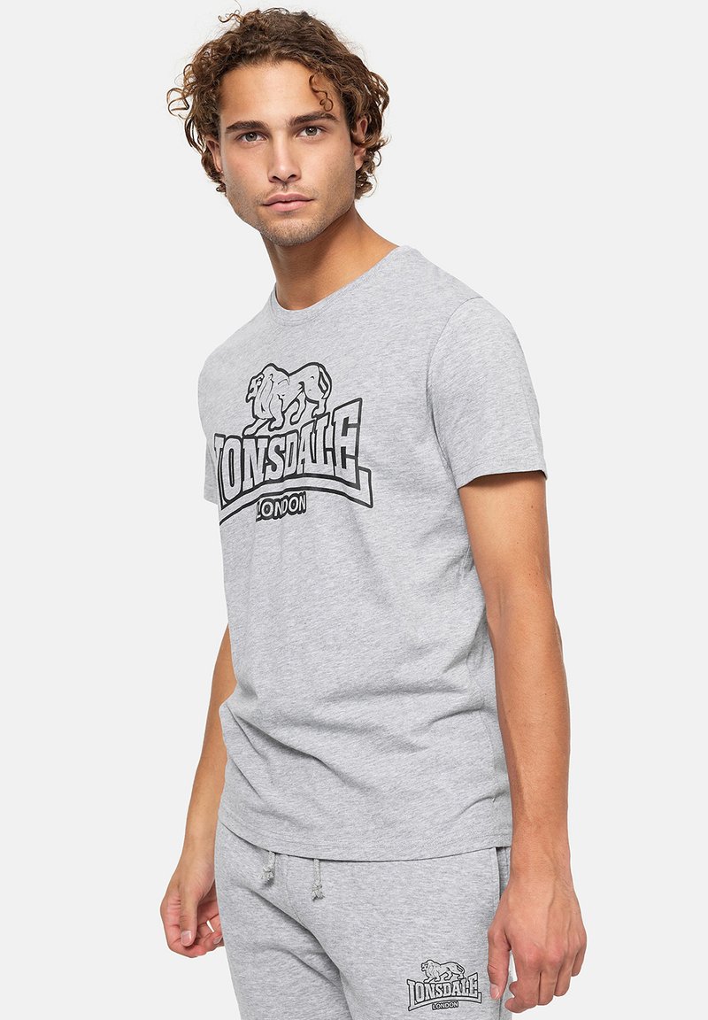 Pelēks kokvilnas T-kreklu ar apaļu kakla izgriezumu, kas rotāts ar melnu lauvu grafiku un tekstu "Lonsdale London". Īsas piedurknes un brīva piegriezuma.