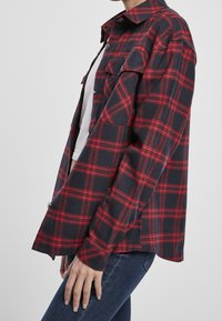 Röd och marinblå rutigt skjorta i avslappnad passform, med två framfickor och knappstängning, tillverkad av ett strukturerat vävt tyg.