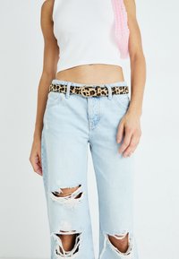 Ανοιχτό μπλε ψηλόμεσα τζιν με σκισίματα στα γόνατα, συνδυασμένα με ζώνη λεοπάρ και λευκό κοντό φανελάκι.