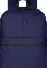 Mörkblå ryggsäck gjord av slitstarkt tyg; har en snygg design, framficka med dragkedja och svarta detaljer samt en logotyp.