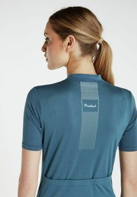 Korte mouwen sporttop in teal met een textuurpatroon. Heeft een logo op de rug en een verticaal streeppatroon langs de wervelkolom.