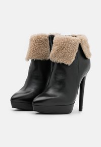 Stivaletti neri in pelle con bordo in ecopelliccia beige, punta affusolata e tacco a stiletto alto. Superficie testurizzata e dettagli della suola in piattaforma.