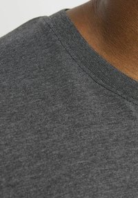 Tejido de camiseta gris oscuro con una textura suave. Cuello redondo con un borde de canalé fino. Vista en primer plano que muestra las costuras y las fibras.