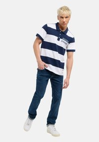 Marinblå och vit randig kortärmad polo med krage, med en liten broderad logotyp. Bärs med mörka jeans och vita sneakers.