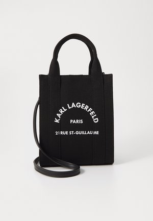 Crna platnena torba s dvostrukim kratkim ručkama i odvojivim kožnim remenom za rame. Ima bijeli natpis s brendom na prednjoj strani.