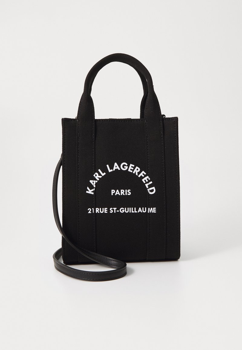 Bolsa de tela negra con asas cortas dobles y una correa de hombro de cuero desmontable. Presenta un logotipo de texto blanco en la parte frontal.