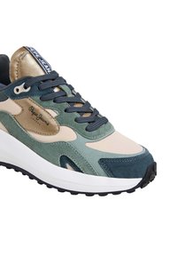 Zapatillas multicolores que presentan una combinación de materiales de gamuza y textil. Los colores incluyen beige, verde y azul marino, con una gruesa suela blanca y una suela exterior negra.